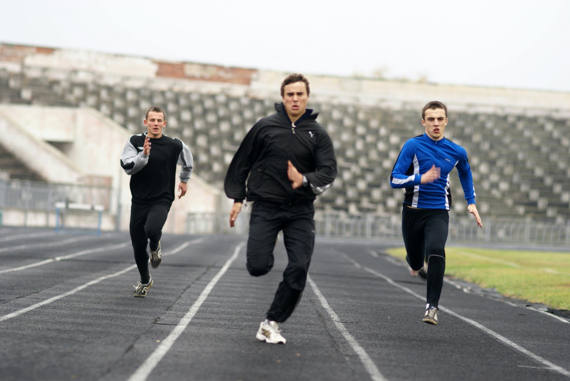 Three regular guys in tracksuits sprinting down a weathered stadium track